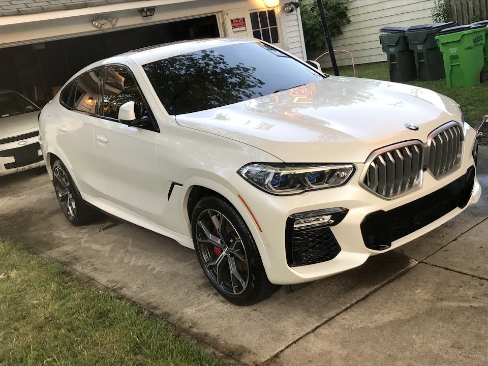 A freshly detailed white BMW SUV parked in a driveway after detailing